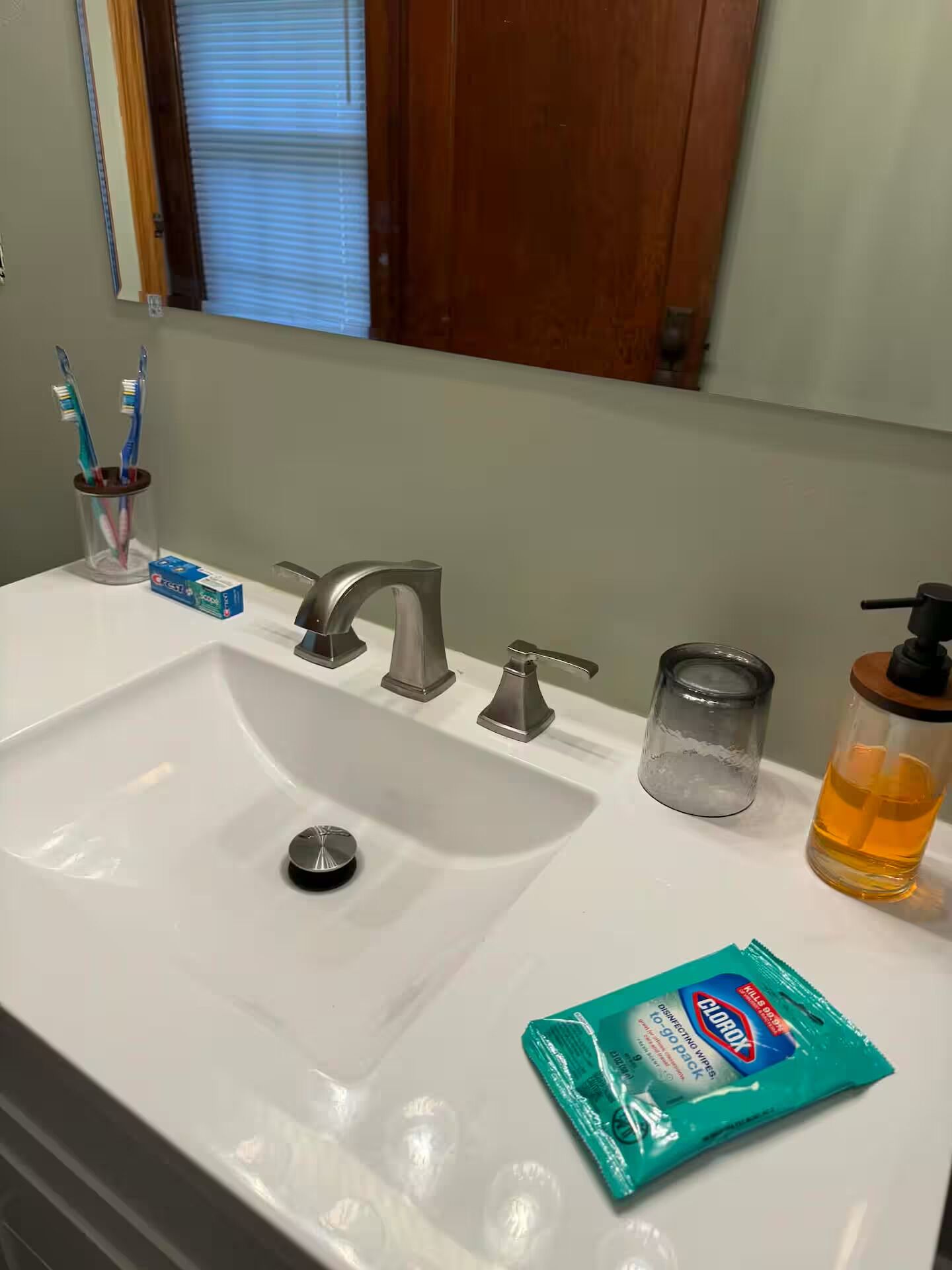 A bathroom sink with a mirror, toothbrush holder, and a pack of Kleenex tissues.