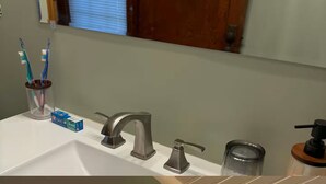 A bathroom with a white sink, two faucets, a soap dispenser, and a toothbrush holder with toothbrushes.
