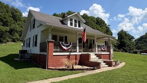 A two-story house with a porch, a brick foundation, and a flag.
