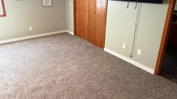 A room with carpeted flooring, a wooden closet, and a mounted flat-screen TV.