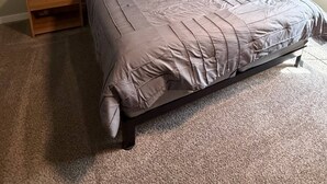 A bedroom with a large bed, two nightstands, a headboard, and a wall-mounted painting.