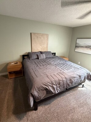 A bedroom with a large bed, two nightstands, a headboard, and a wall-mounted painting.
