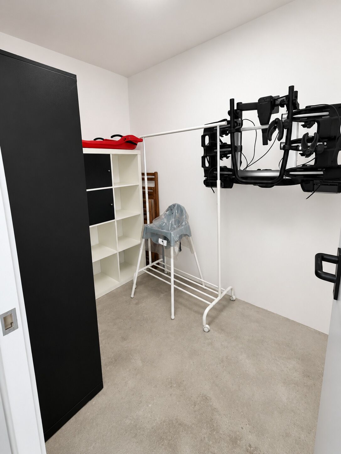 Une pièce avec une armoire blanche, un étendoir métallique et une porte noire.
