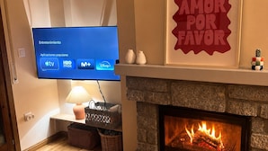 A living room with a flat-screen TV displaying popular apps, a fireplace, a framed motivational quote, and a round wooden table.