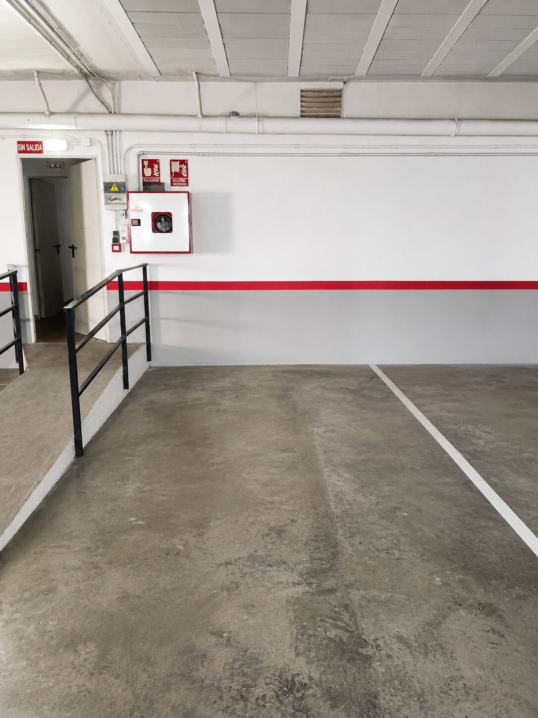 An empty parking garage with a concrete floor, a red safety line, and a fire extinguisher mounted on the wall.