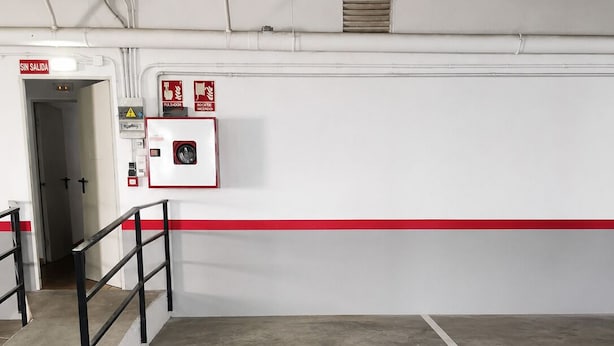 An empty parking garage with a concrete floor, a red safety line, and a fire extinguisher mounted on the wall.