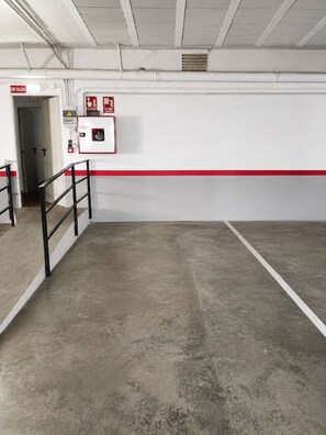 An empty parking garage with a concrete floor, a red safety line, and a fire extinguisher mounted on the wall.