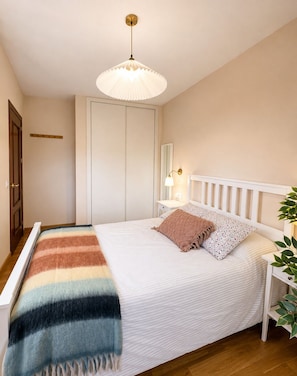 A bedroom with a bed, bedside table, lamp, and a hanging light fixture.