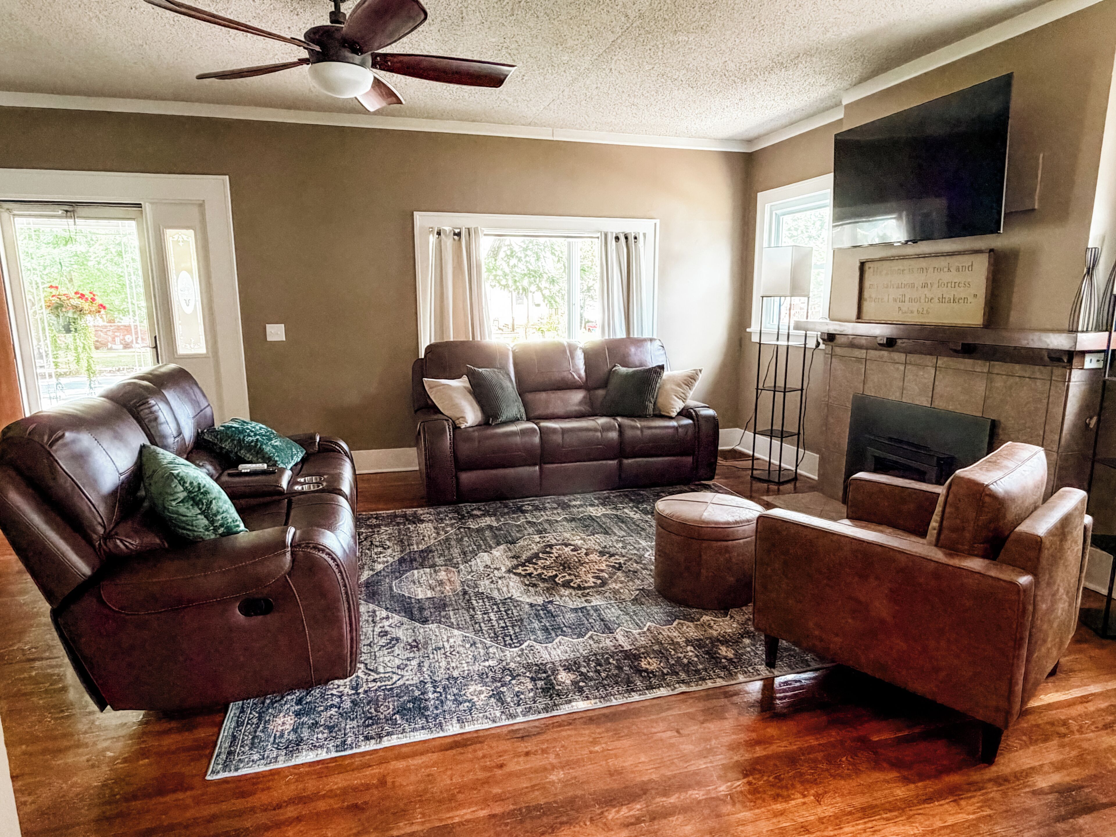 A living room with a brown leather sofa, a matching armchair, a patterned rug, a ceiling fan, and a fireplace.