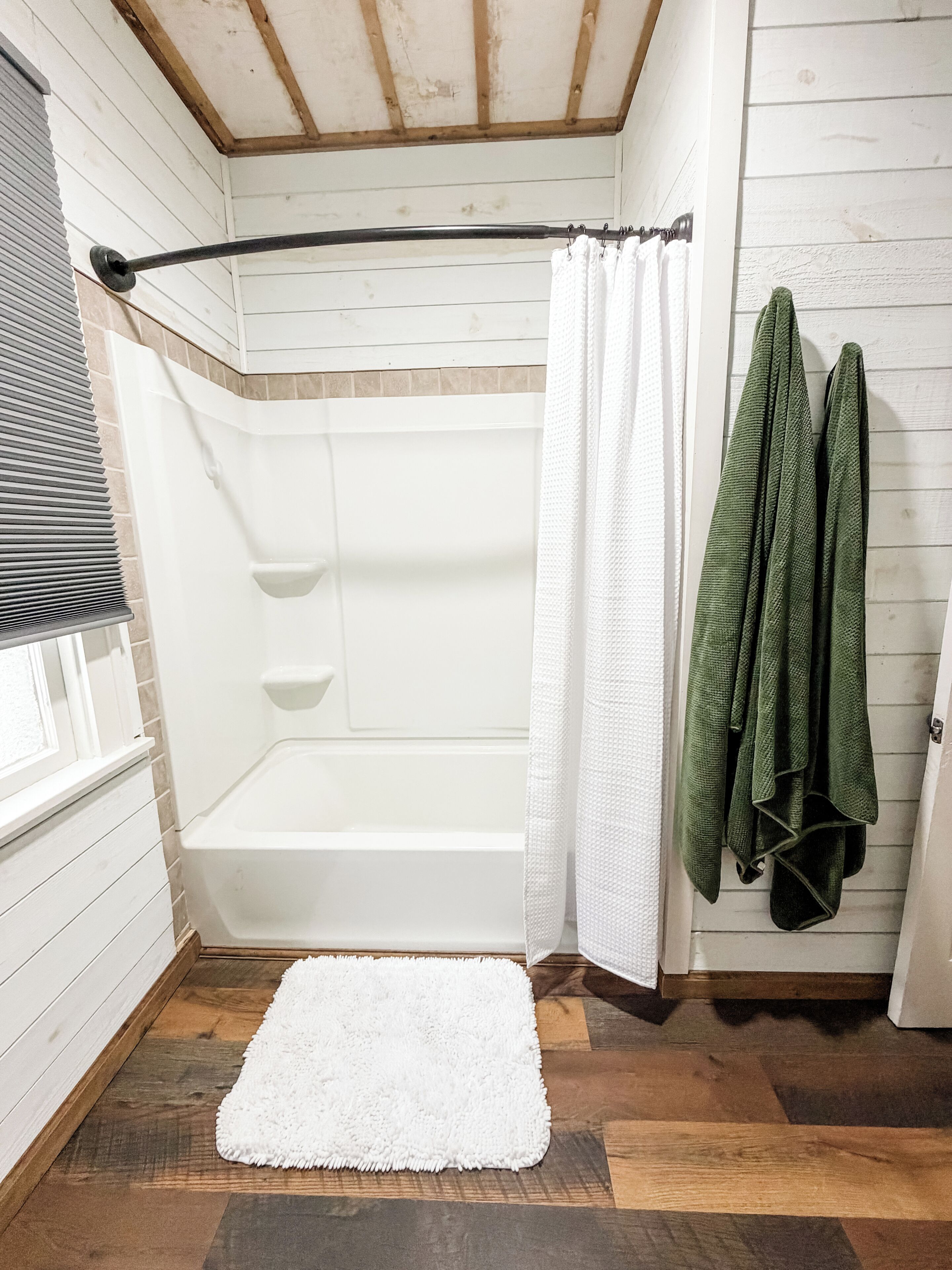 A bathroom with a white bathtub, a shower curtain, and a white rug on the floor.