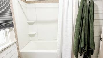 A bathroom with a white bathtub, a shower curtain, and a white rug on the floor.