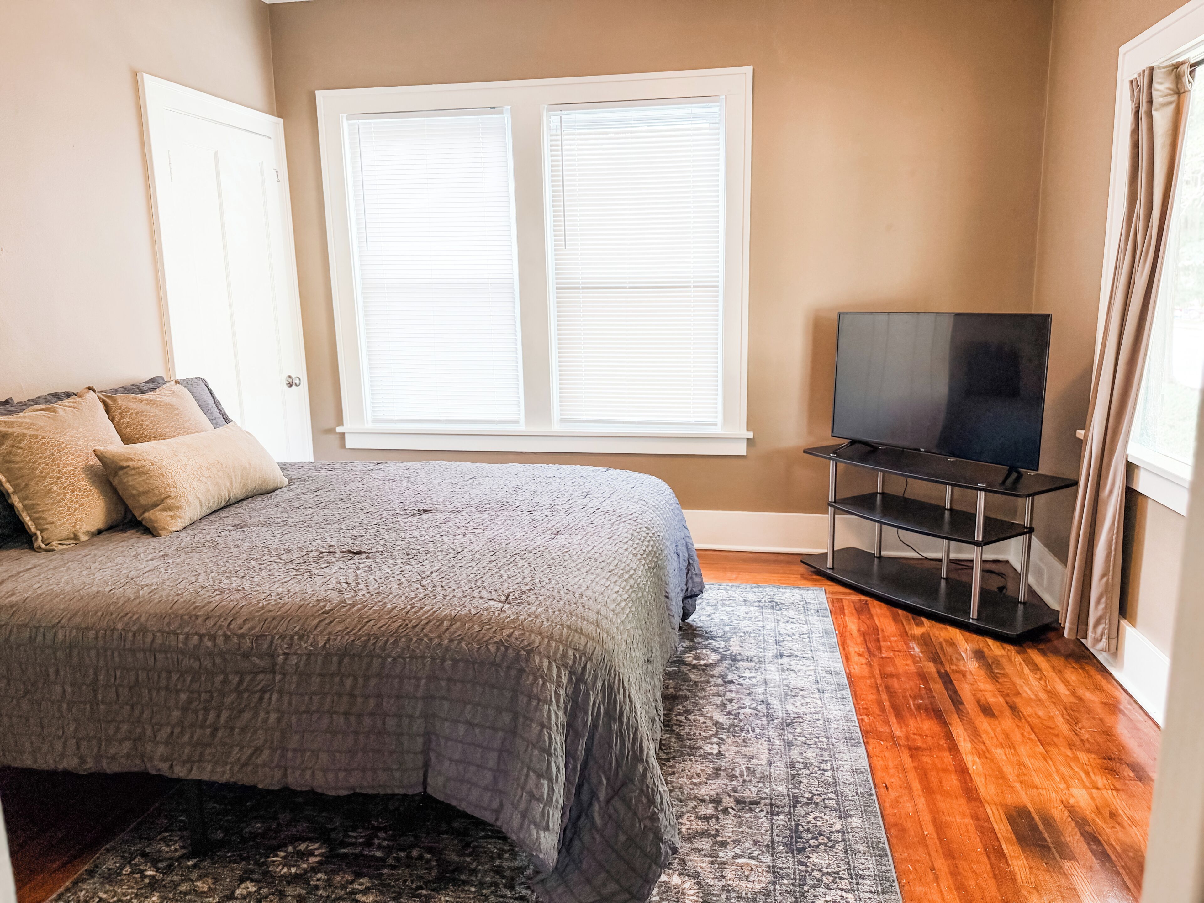 A bedroom with a bed, a television on a stand, and a window with blinds.