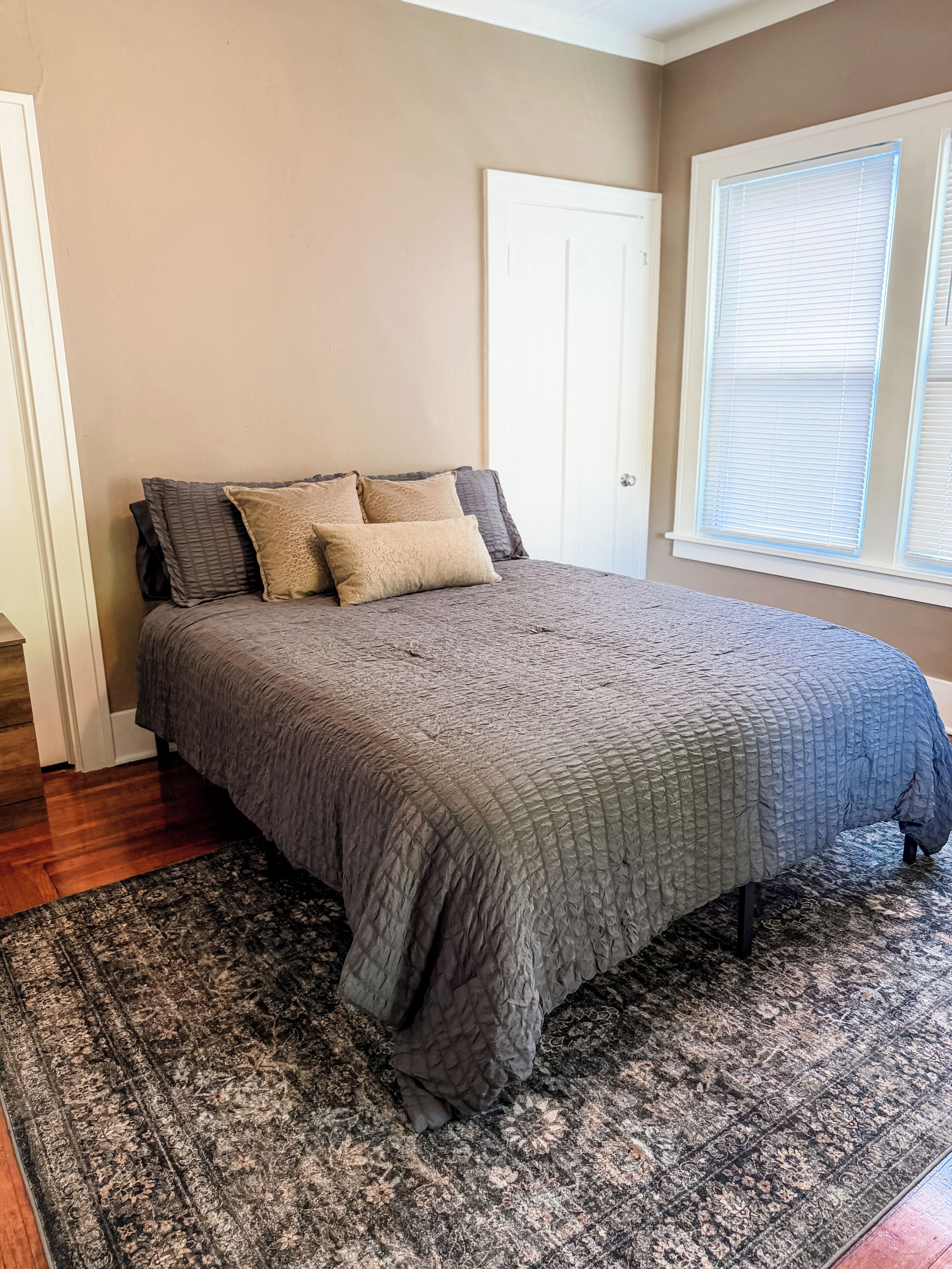 Une chambre à coucher avec un lit, un tapis à motifs, une porte et une fenêtre avec des stores.