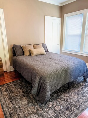 A bedroom with a bed, a patterned rug, a door, and a window with blinds.