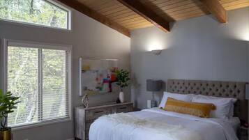 Ein Schlafzimmer mit großem Fenster, einem Bett mit weißer Bettwäsche, einem Kopfteil und einem Nachttisch mit Lampe.