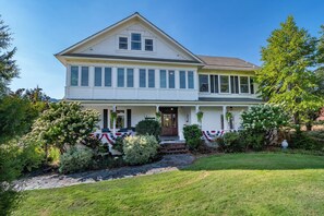 A two-story house with a front porch, a stone pathway, and a well-maintained lawn. - C.H. Bailey House - Brenner Suite (Roseburg)