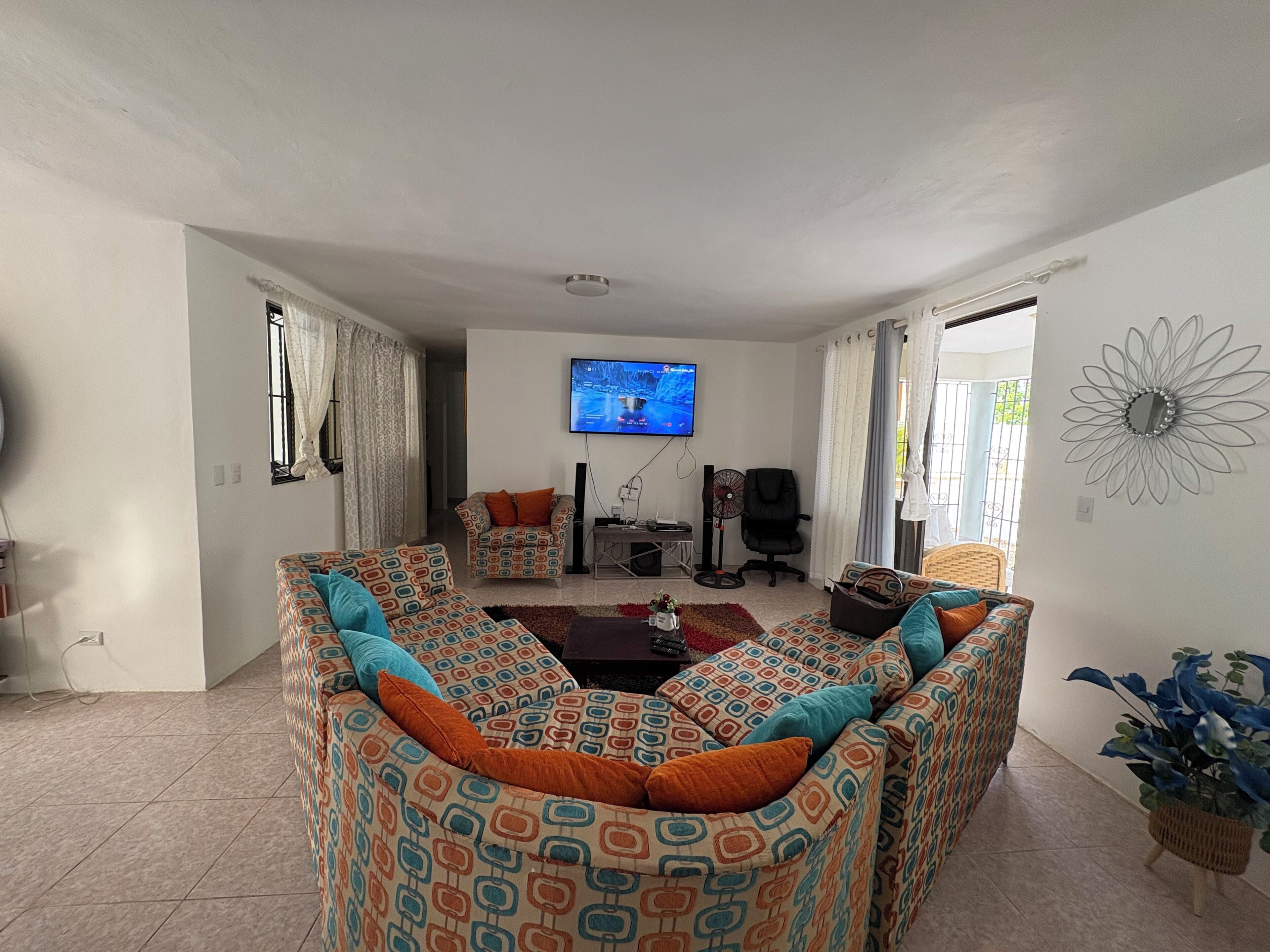 Een woonkamer met gestoffeerde banken met een patroon, een televisie, een ventilator en een decoratief wandobject.