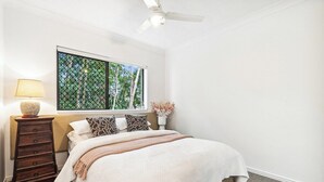 Ein Schlafzimmer mit einem Bett, einer Kommode, einem Fenster mit Blick auf Bäume und einem Deckenventilator.