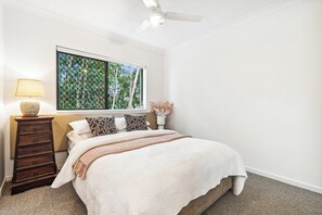Ein Schlafzimmer mit einem Bett, einer Kommode, einem Fenster mit Blick auf Bäume und einem Deckenventilator.