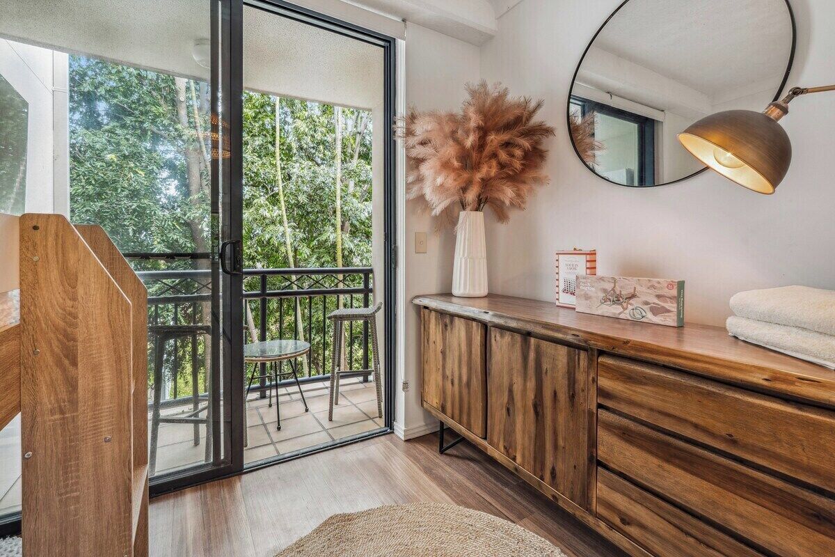 Quarto com porta de vidro deslizante para uma varanda, um armário de madeira, um espelho e um vaso com plantas secas.