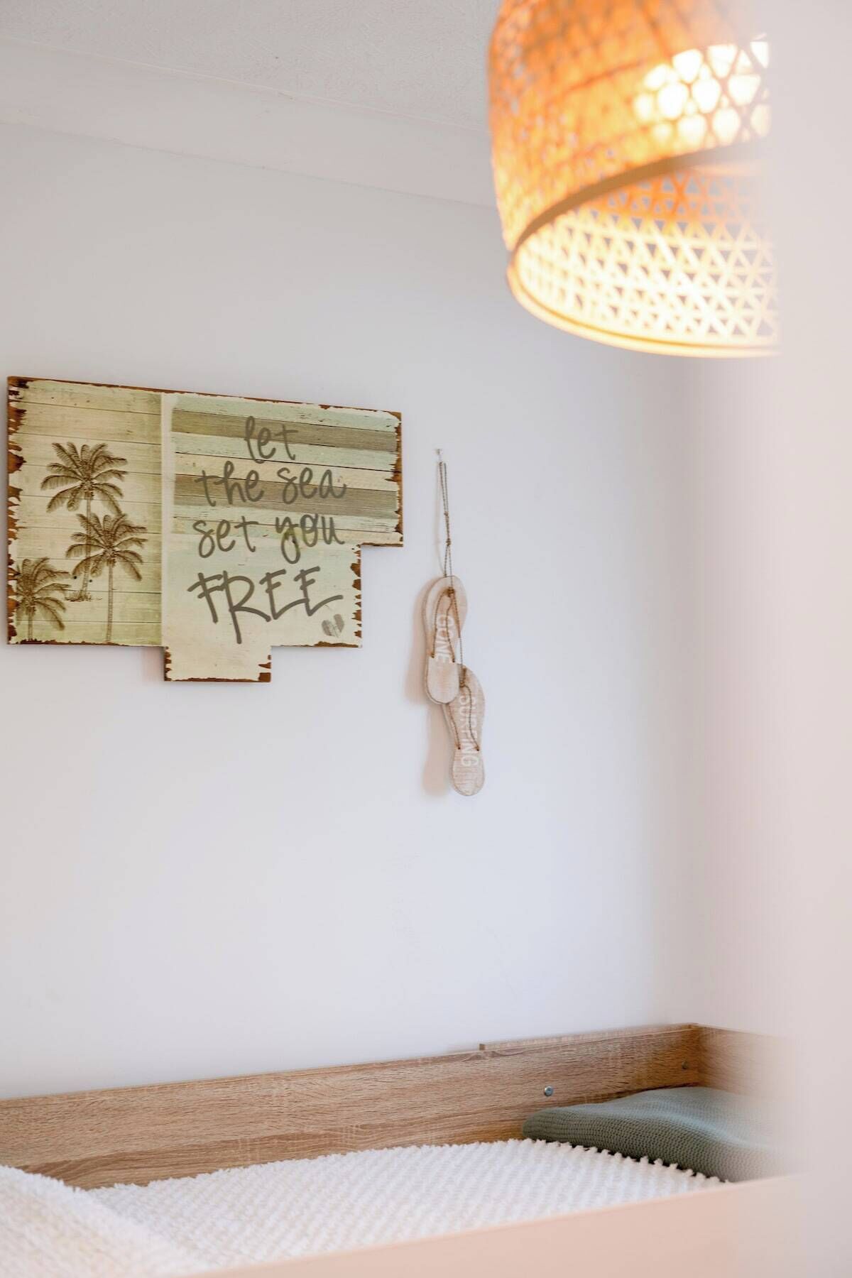 Una habitación con cama, lámpara de pared y un adorno con palmeras y la frase 'let the sea set you free'.