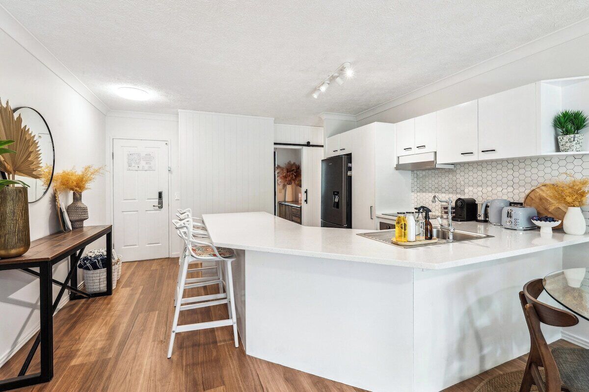 Een moderne keuken met witte kasten, een groot eiland en een eethoek met een glazen tafel.