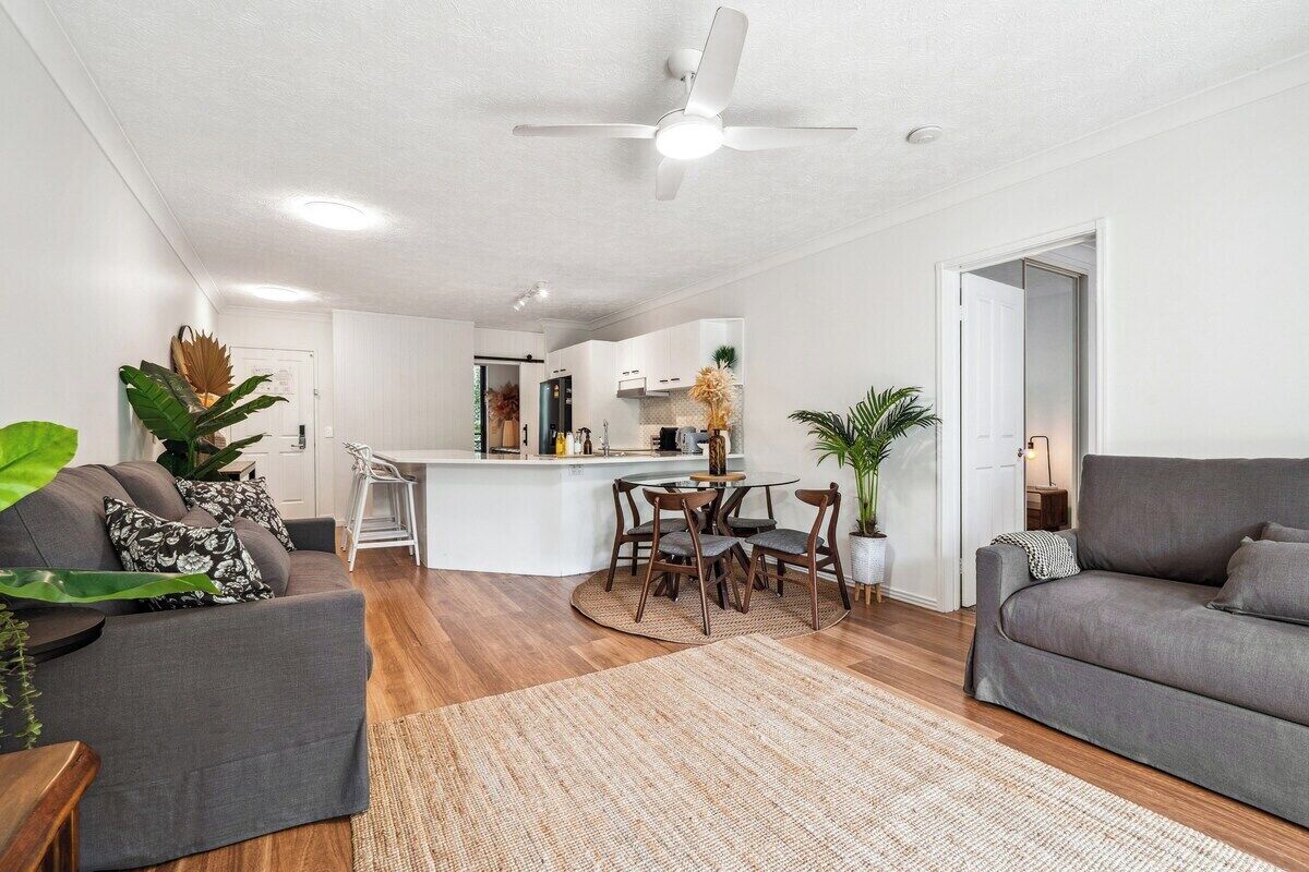 A modern living room with a grey sofa, a dining area with a round table, and a kitchen in the background.