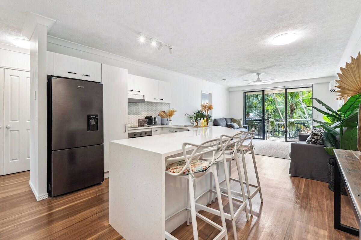 A modern kitchen with a central island, bar stools, and a large refrigerator.