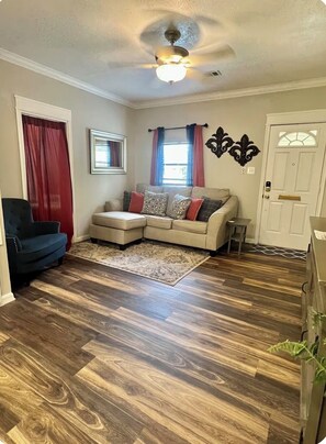 A living room with a sectional sofa, a ceiling fan, a patterned rug, and a door with a decorative handle.