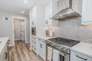 A modern kitchen with white cabinetry, a stainless steel stove, and a hexagonal tile backsplash. - Spring Creek Getaway, Luxury 1BR Condo in Canmore (Canmore)