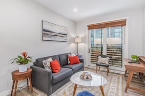 A modern living room with a grey sofa, a coffee table, a side table with a plant, and a view through a glass door. - Spring Creek Getaway, Luxury 1BR Condo in Canmore (Canmore)
