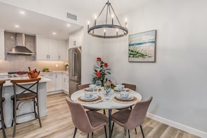 A modern kitchen with white cabinetry, a stainless steel refrigerator, and a dining area with a round table set for four. - Spring Creek Getaway, Luxury 1BR Condo in Canmore (Canmore)