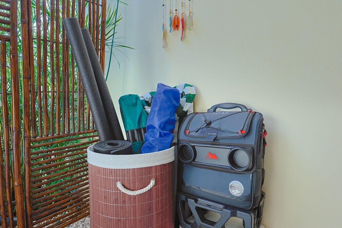 Ein Bambuszaun, eine Aufbewahrungsbox mit Gegenständen und ein schwarzer Koffer an einer Wand.