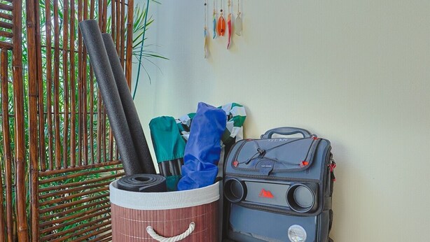 Une clôture en bambou, un bac de rangement contenant divers objets et une valise noire appuyée contre un mur.
