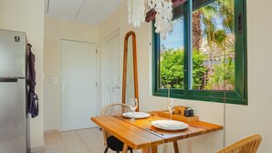 Une cuisine compacte équipée d’un réfrigérateur, d’une table à manger avec des chaises et d’une fenêtre donnant sur un espace verdoyant.