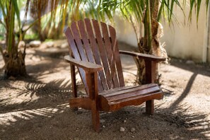 A wooden Adirondack chair in a natural setting with palm trees and a dirt ground. - Coco Cottage Tropical 1BR Near Palm & Eagle Beach (Noord)