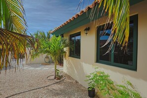 Un bâtiment avec un toit en tuiles, une cour en gravier et un petit palmier.