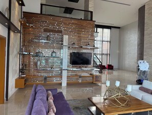 Een moderne woonkamer met een flatscreen televisie, een houten lattenwand, een paarse bank en een salontafel met decoratieve objecten.