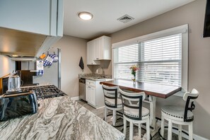 A kitchen with a marble countertop, white cabinets, a dining table with chairs, and a window with blinds. - Lighthouse Lookout - Cozy 2-bedroom condo in Lighthouse District Brigantine, NJ (Brigantine)