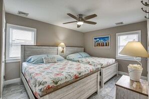 Ein Schlafzimmer mit zwei Betten, einem Deckenventilator, einem Strandbild und einer Lampe auf einem Nachttisch.