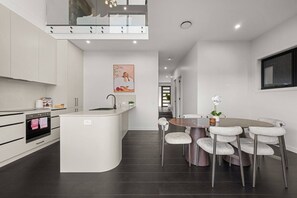 A modern kitchen with a central island, a dining area with a round table and cushioned chairs, and a staircase leading to an upper level. - Premium 3BR Snowy Mountains Retreat w/ Ducted A/C! (Jindabyne)