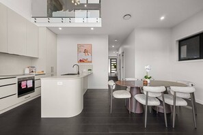 A modern kitchen with a central island, a dining area with a round table and cushioned chairs, and a staircase leading to an upper level. - Premium 3BR Snowy Mountains Retreat w/ Ducted A/C! (Jindabyne)