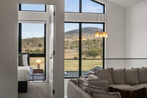 Ein Zimmer mit großem Fenster, einer Couch, einem Nachttisch und einer Lampe.