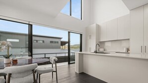 Eine moderne Küche mit weißen Schränken, ein Essbereich mit einem Glastisch und Blick auf ein Gebäude.