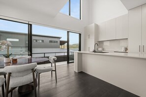 Eine moderne Küche mit weißen Schränken, ein Essbereich mit einem Glastisch und Blick auf ein Gebäude.