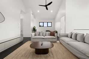 A modern living room with a sofa, a coffee table, and a ceiling fan. - Snowy Mountains Retreat with Indoor Fireplace (Jindabyne)