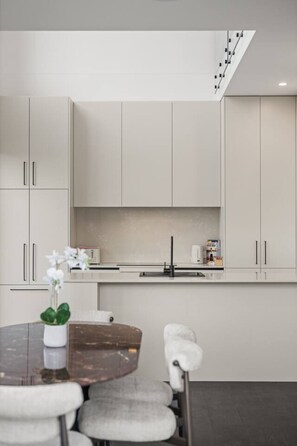 A modern kitchen with white cabinets, a dark countertop, and a staircase leading to an upper level. - Snowy Mountains Retreat with Indoor Fireplace (Jindabyne)