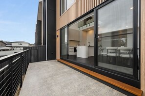 A modern building with a balcony, large windows, and a visible kitchen area. - Snowy Mountains Retreat with Indoor Fireplace (Jindabyne)