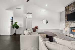 Een moderne woonkamer met een stenen haard, een grote spiegel en een hoekbank.