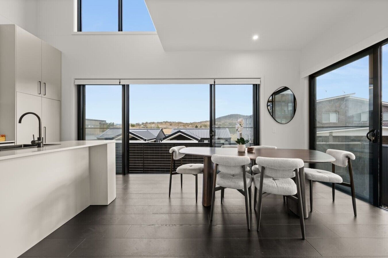A modern kitchen with a dining area, large windows, and a view of the surrounding area.